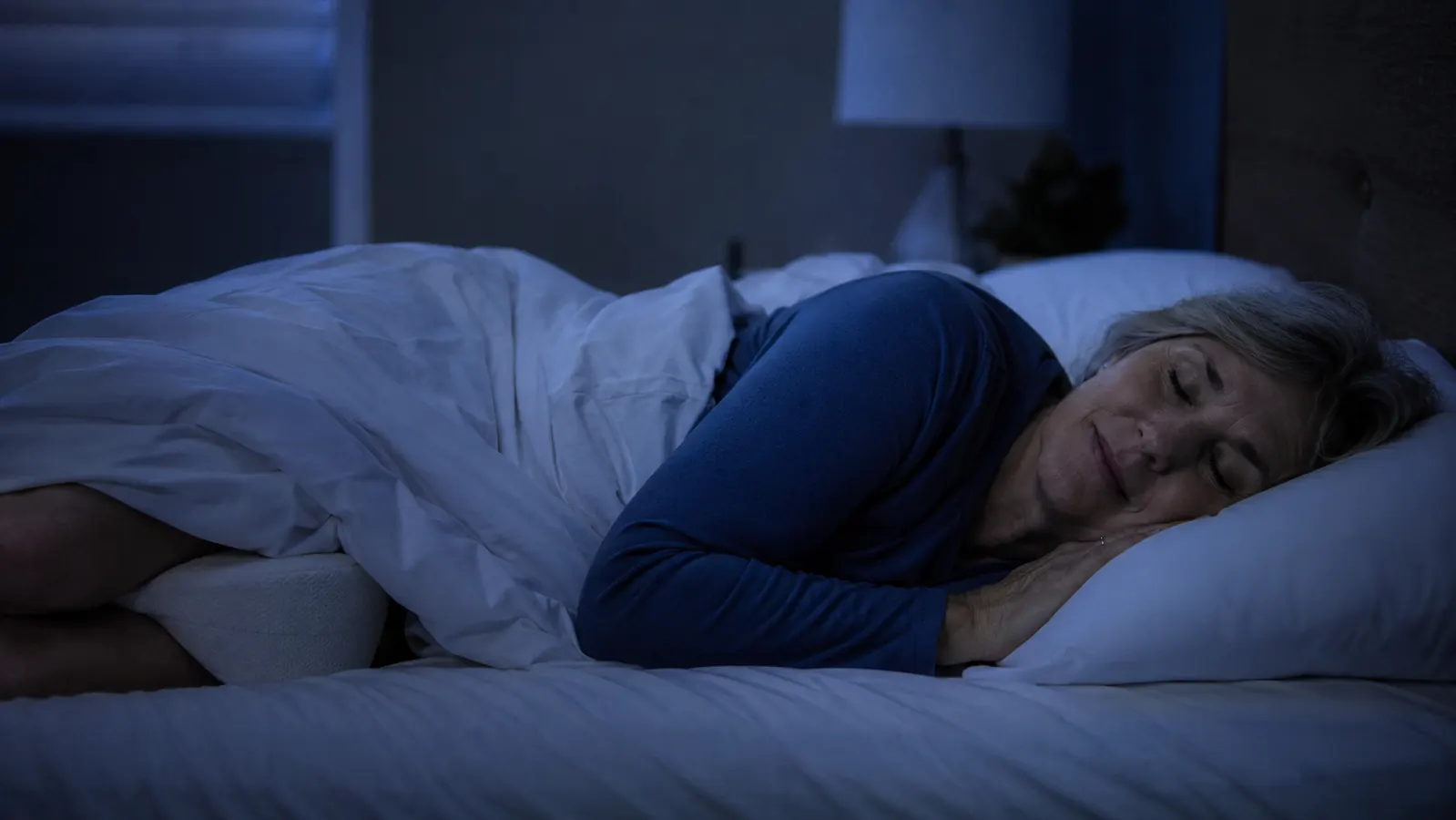 Woman sleeping peacefully through the night with a knee pillow in place, dark bedroom, undisturbed